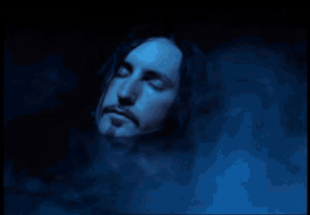 a man with dreadlocks and a beard is laying in a dark room with his eyes closed .
