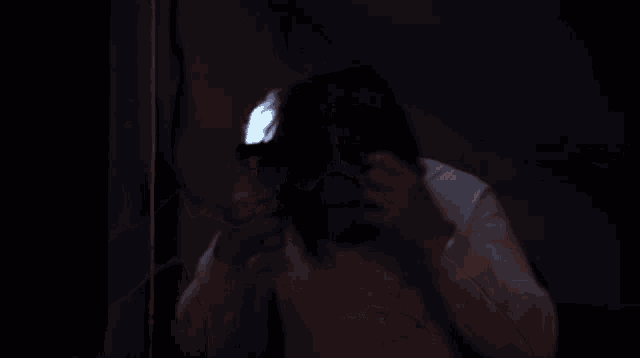 a man with long hair and a beard is standing in a dark room with a light shining on him