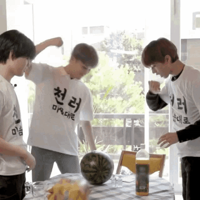 a group of young men wearing white shirts with korean writing on them are playing with a watermelon