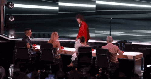 a man in a red tuxedo is standing on a stage in front of a crowd
