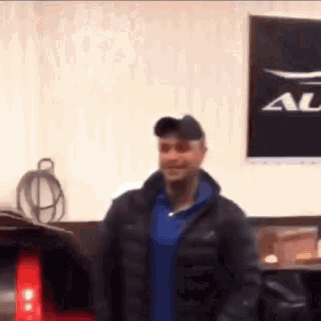 a man wearing a black jacket and a blue shirt is standing in front of a sign that says a on it .