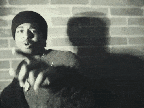 a black and white photo of a man wearing a beanie pointing at the camera