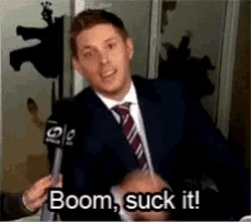 a man in a suit and tie is holding a microphone and says boom suck it .