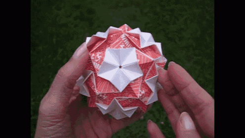 a person is holding a red and white origami sphere