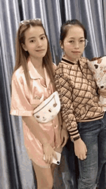 two women are posing for a picture in front of a curtain . one of the women is holding a bouquet of flowers .