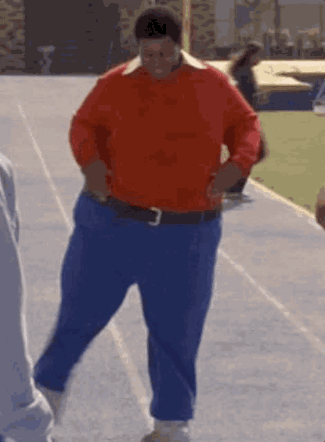 a man wearing a red sweater and blue pants is walking on a track .