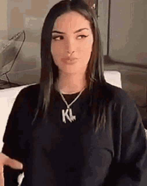 a woman wearing a black shirt and a necklace is sitting on a couch and looking at the camera .