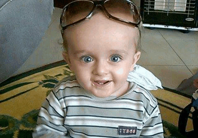 a baby wearing sunglasses and a striped shirt is sitting on the floor .