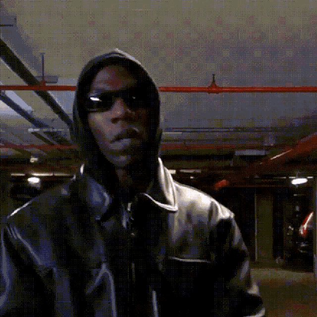 a man wearing sunglasses and a hooded jacket in a dark room
