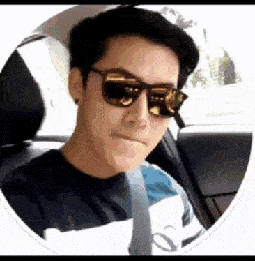 a man wearing sunglasses is sitting in a car and making a face .