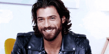 a man with long hair and a beard wearing a leather jacket is smiling .