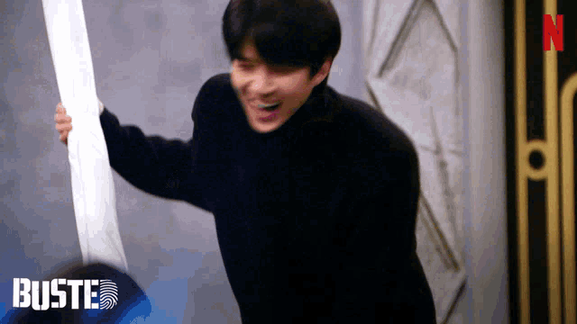 a man in a black turtleneck is holding a piece of paper in front of a sign that says buste