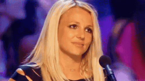 britney spears is sitting in front of a microphone and looking at the camera .