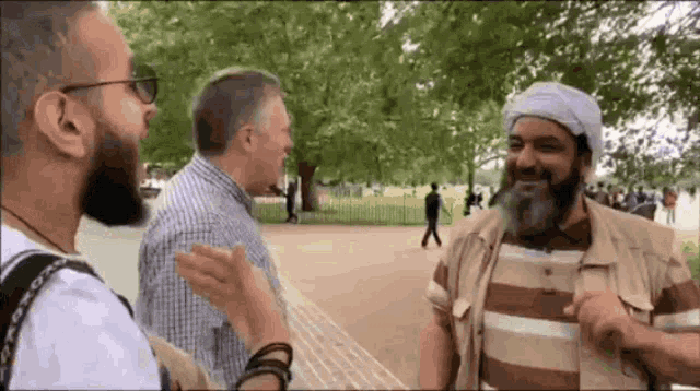 a man with a beard is talking to two other men in a park