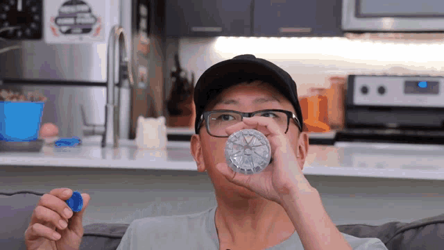 a man wearing glasses and a hat is drinking from a clear bottle