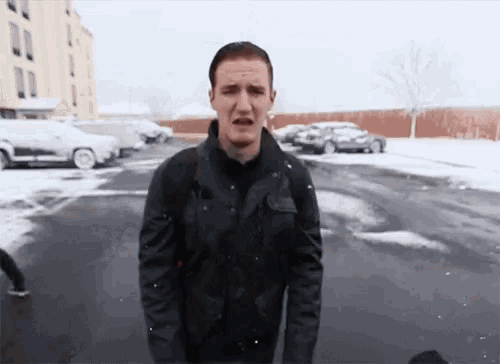 a man in a black jacket is standing in a parking lot with snow on the ground