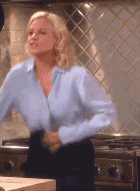 a woman in a blue shirt is standing in front of a kitchen stove