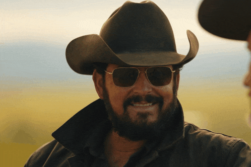 a man in a cowboy hat and sunglasses smiles
