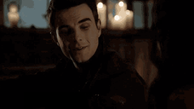 a young man is sitting in a dark room with candles in the background and smiling .