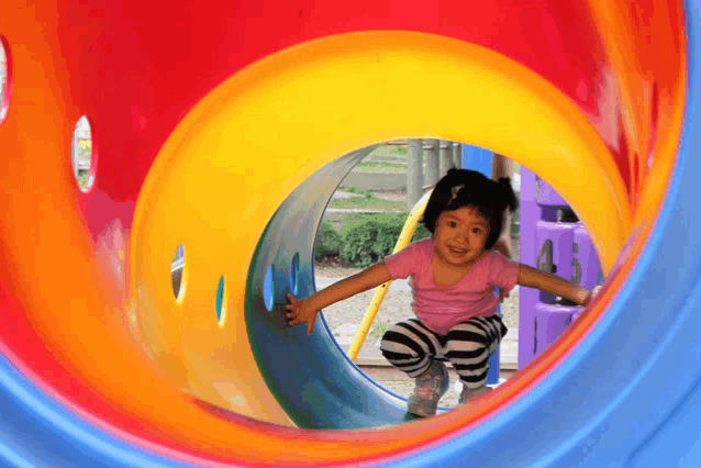 a little girl in a pink shirt is playing in a colorful tunnel