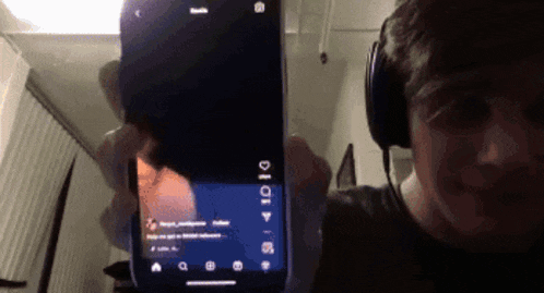 a man wearing headphones is holding up a cell phone with a screen that says ' i ' on it