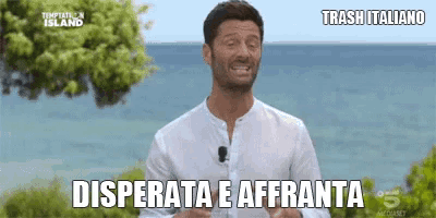 a man in a white shirt stands in front of the ocean and says desperata e affranta .
