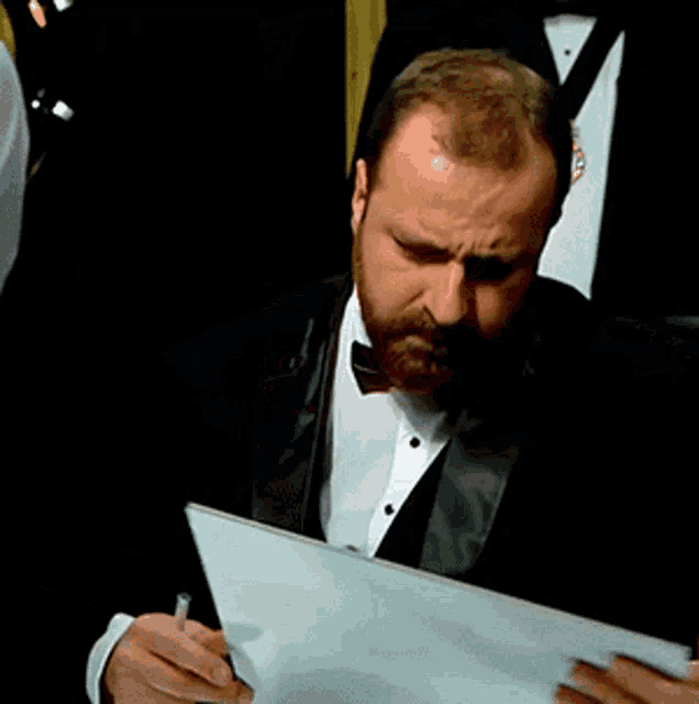 a man in a tuxedo with a beard is writing on a piece of paper