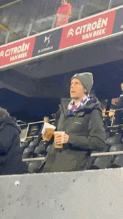 a man is sitting in a stadium holding a cup of beer