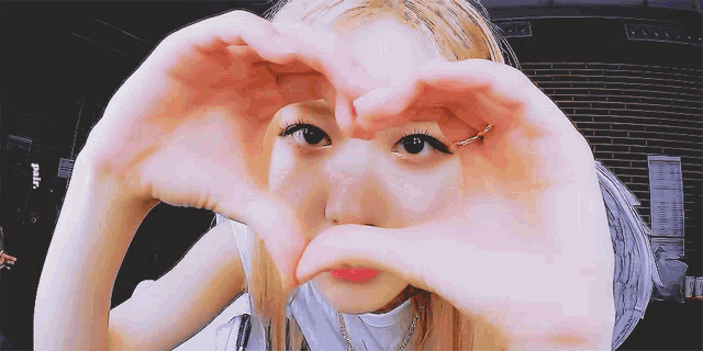 a woman making a heart with her hands in front of her eyes