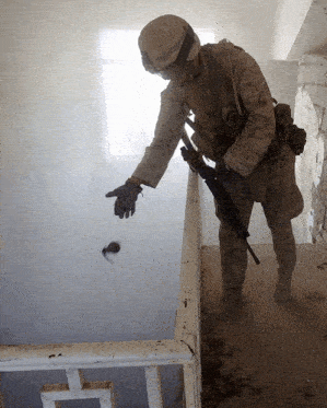 a soldier reaches for a grenade that is flying through the air
