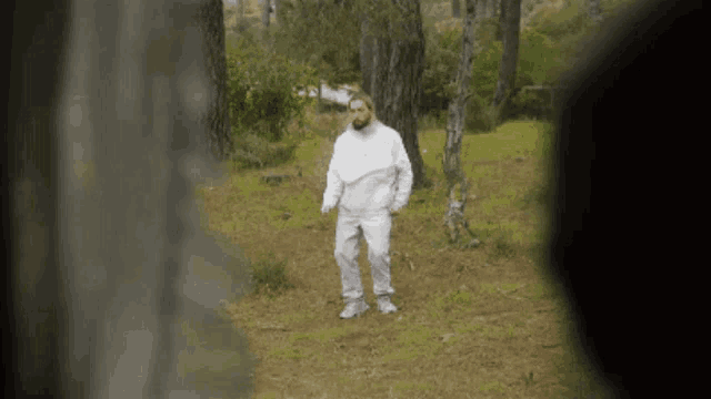 a man in a white outfit is standing in a forest .