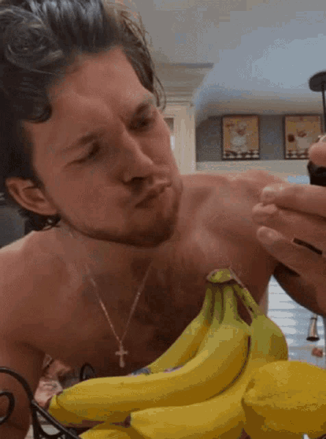 a shirtless man looks at a bunch of bananas in a basket
