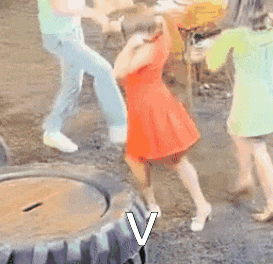 a group of people are dancing in front of a tire with the letter v in the corner .