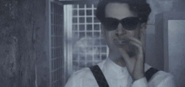 a man wearing sunglasses and suspenders is standing in a dark room .
