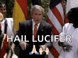 a man in a suit and tie is standing in front of flags with the words hail lucifer written above him .