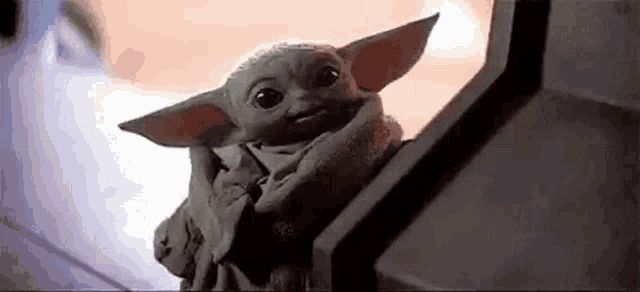 a baby yoda from star wars is sitting on a set of stairs and looking at the camera .
