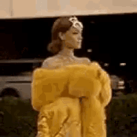 a woman in a yellow dress with a tiara on her head is standing in front of a building .