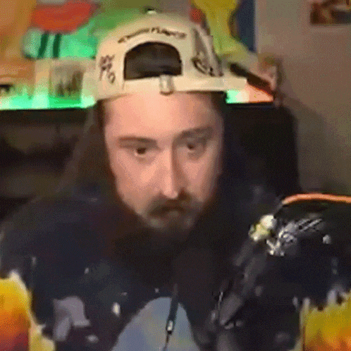 a man with a beard wearing a hat and a hoodie is sitting in front of a computer .