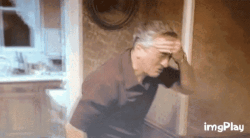 an older man is leaning against a wall while holding his head .
