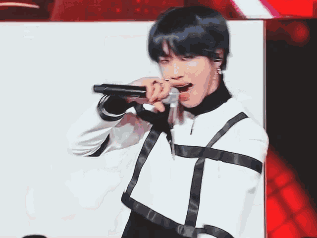 a man with blue hair is singing into a microphone while wearing a black and white outfit