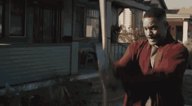 a man in a red robe is holding a large stick in his hand in front of a house .