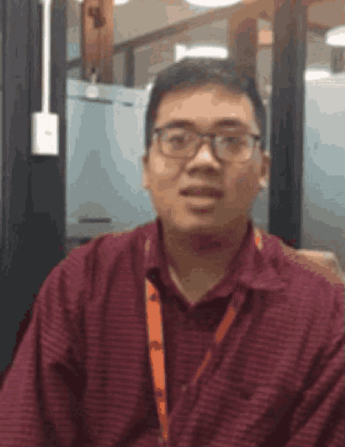a man wearing glasses and a red shirt is sitting in front of a glass wall .