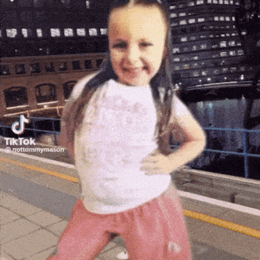 a little girl in a white shirt and pink skirt is dancing on a platform with a tiktok watermark