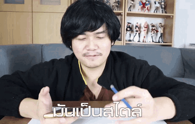 a man sitting at a table with a pencil in his hand and a foreign language written on the bottom of the image