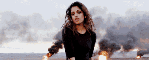 a woman in a black dress is standing in front of a fire