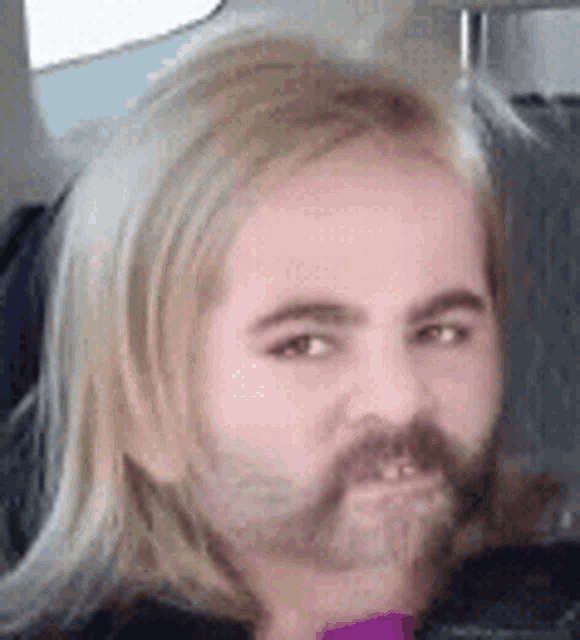 a man with blonde hair and a beard is sitting in a car .