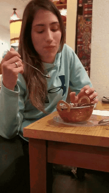a woman wearing a blue under armour shirt is sitting at a table eating food