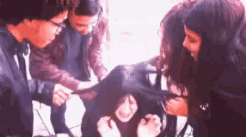 a group of people are standing around a woman 's head and talking to her .