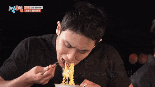 a man in a black shirt is eating noodles with chopsticks from a bowl