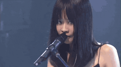 a woman with long black hair is singing into a microphone .